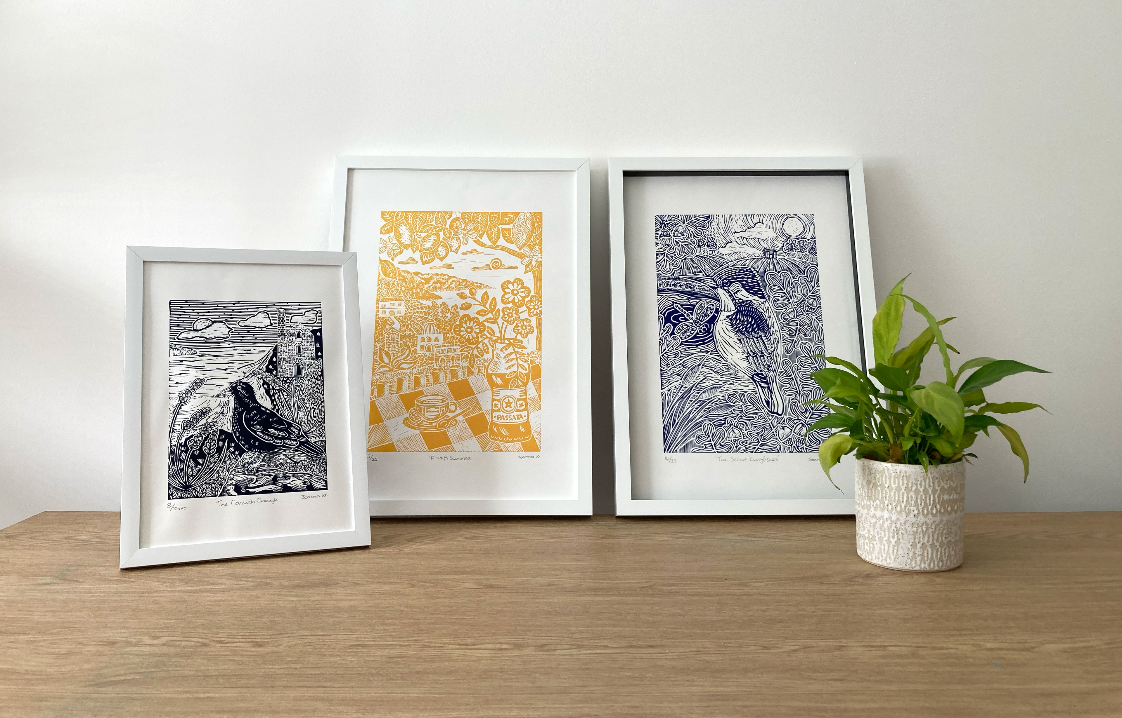 Three framed lino prints on a wooden surface with a plant in the background by Joanna Williams Art - lino print artist Cornwall