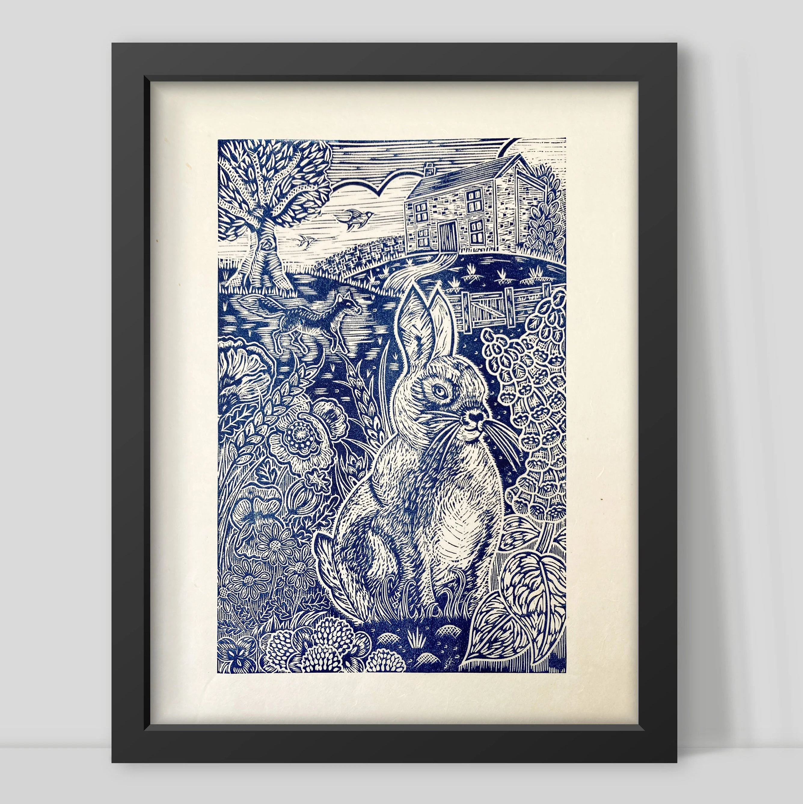 Framed artwork with a blue and white design of a rabbit and landscape by Joanna Williams Art - lino printer.