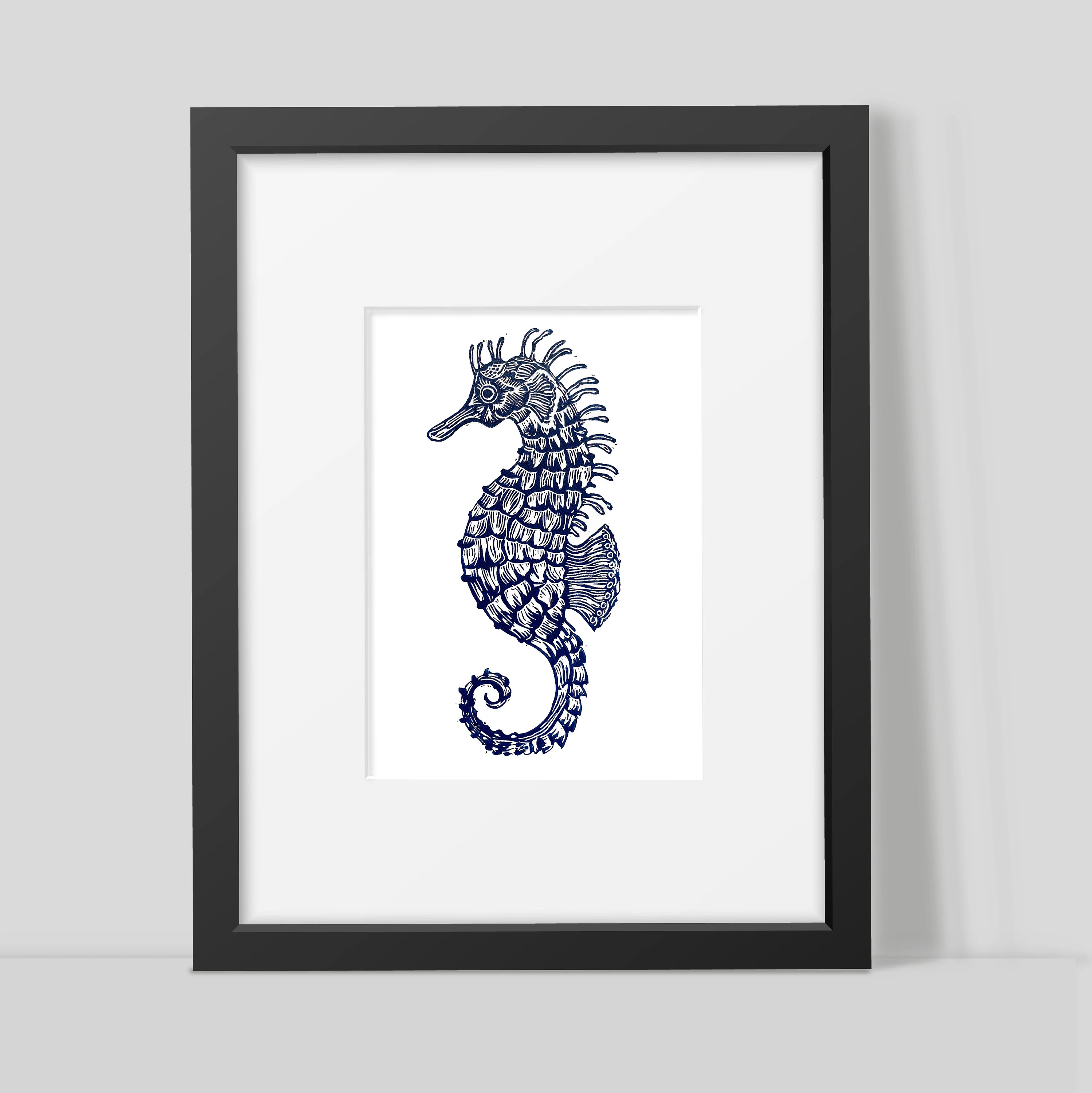 Framed artwork of a blue seahorse on a white background by Joanna Williams Art - lino printer.